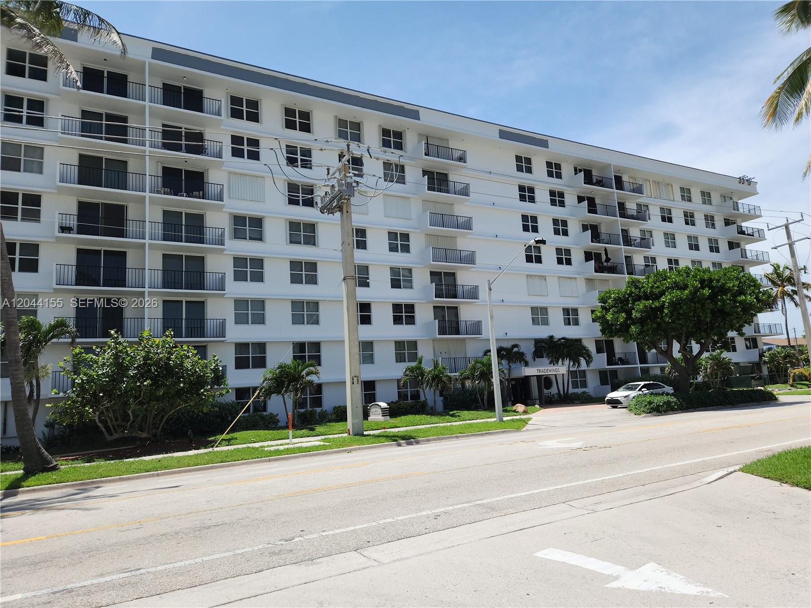 A multi-story white apartment building stands along a street with palm trees and landscaping — 1009 N Ocean Blvd # 411, Pompano Beach FL 33062, POMPANO BEACH, FL