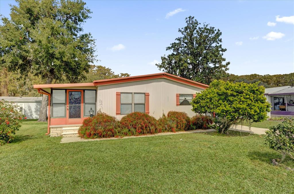 A single-story manufactured home with light siding, orange trim, and a front screen porch — 415 S TIMBER TRAIL, WILDWOOD, FL