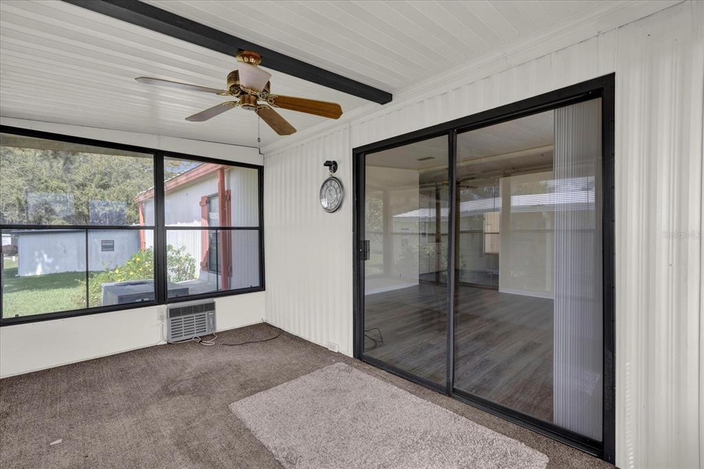 A screened-in porch features a ceiling fan, carpeted flooring, and a sliding glass door — 415 S TIMBER TRAIL, WILDWOOD, FL