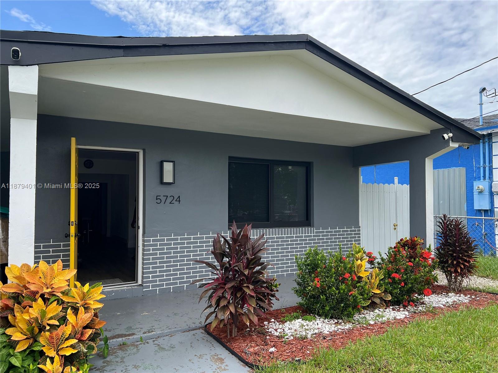 A gray house exterior features a yellow door, white brick accents, and a landscaped garden — 5724 SW 18th St, West Park FL 33023, WEST PARK, FL