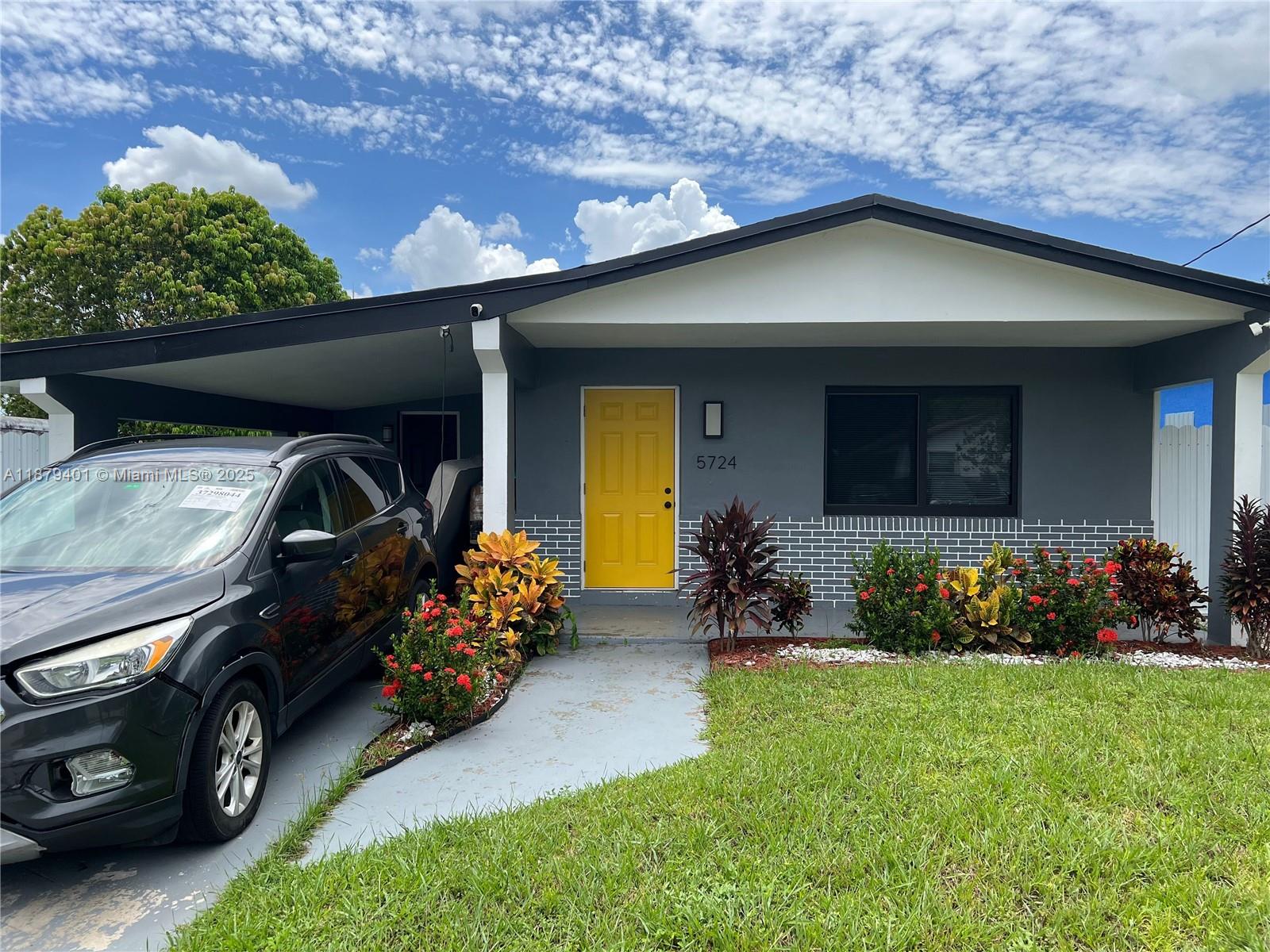 A gray house with a yellow front door and a carport sits behind a lawn — 5724 SW 18th St, West Park FL 33023, WEST PARK, FL