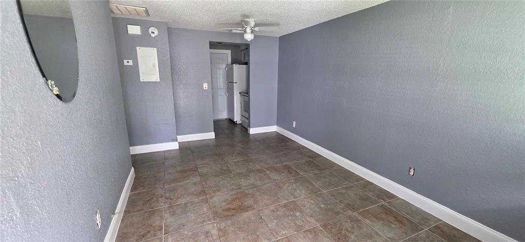 An empty room with gray walls, tile flooring, a ceiling fan, and an adjacent kitchen — 1308 E YUKON STREET UNIT B, TAMPA, FL