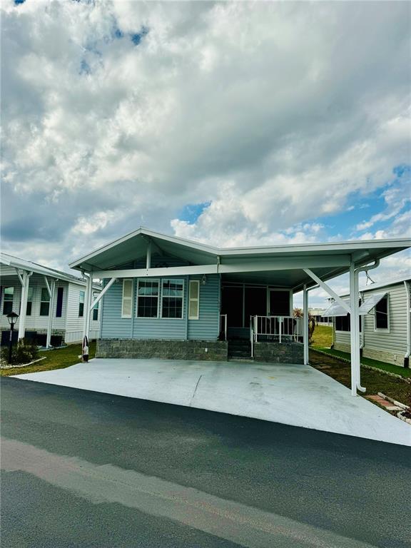 A light blue manufactured home features a large attached carport and a concrete driveway — 603 ARNOLD PALMER DRIVE, DAVENPORT, FL