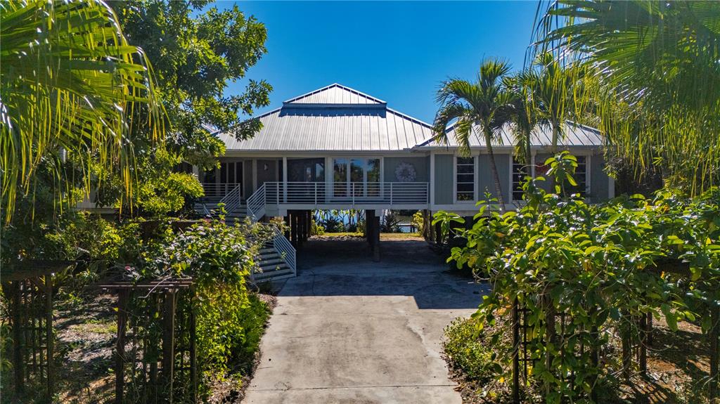 An elevated house with a metal roof stands at the end of a concrete driveway — 24139 JOLLY ROGER BOULEVARD, PUNTA GORDA, FL