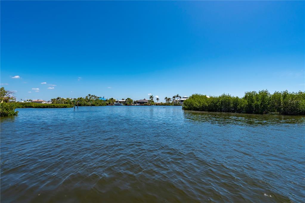 A view of a calm waterway surrounded by mangroves with houses visible in the distance — 24139 JOLLY ROGER BOULEVARD, PUNTA GORDA, FL