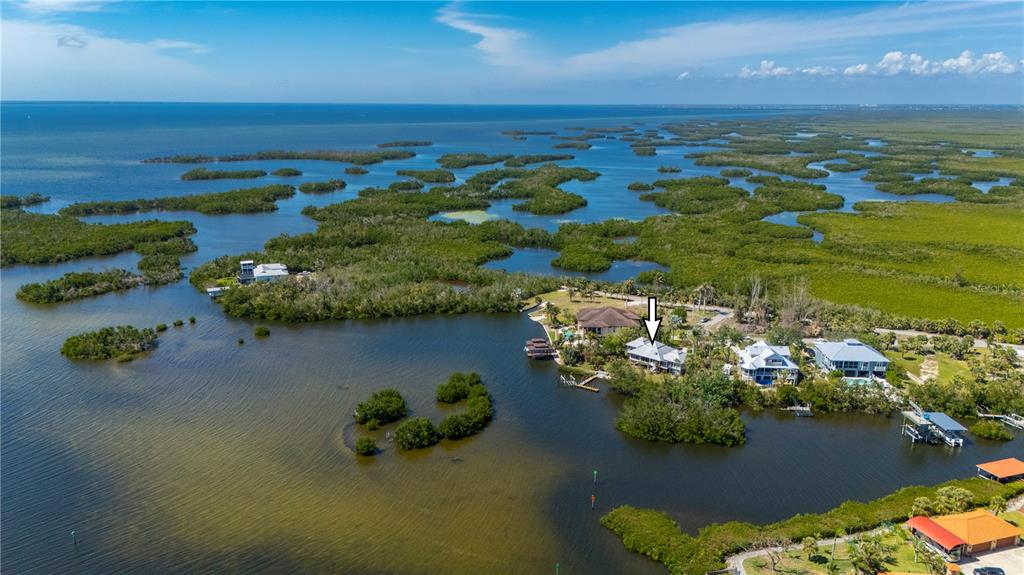 An aerial view shows a waterfront house with a white arrow pointing to its roof — 24139 JOLLY ROGER BOULEVARD, PUNTA GORDA, FL