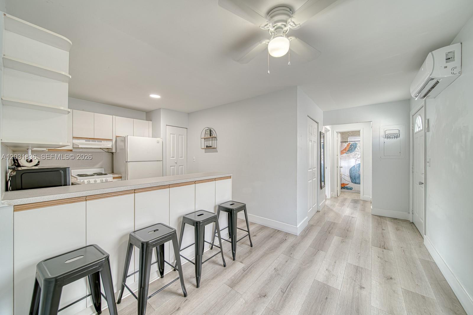 A kitchen with white cabinets, a breakfast bar with three stools, and light wood flooring — 7622 SW 21st St # 7622, Miami FL 33155, MIAMI, FL