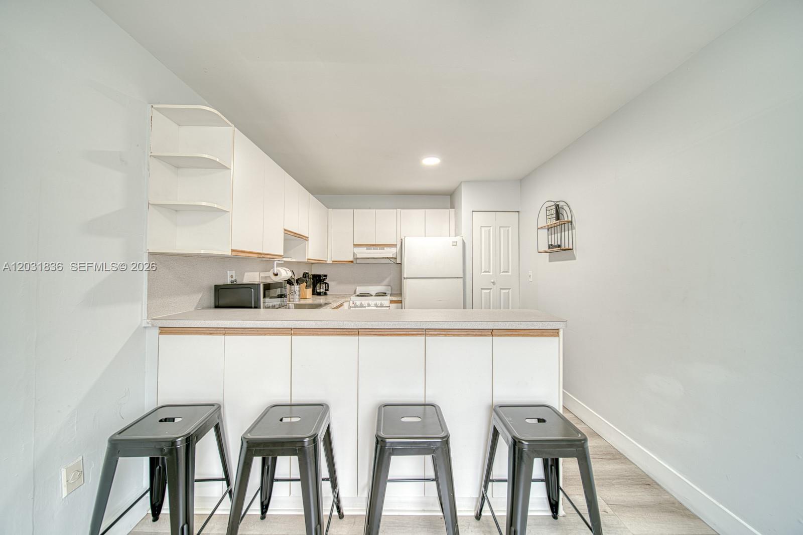 A kitchen features white cabinets, a breakfast bar with four stools, and light-colored flooring — 7622 SW 21st St # 7622, Miami FL 33155, MIAMI, FL