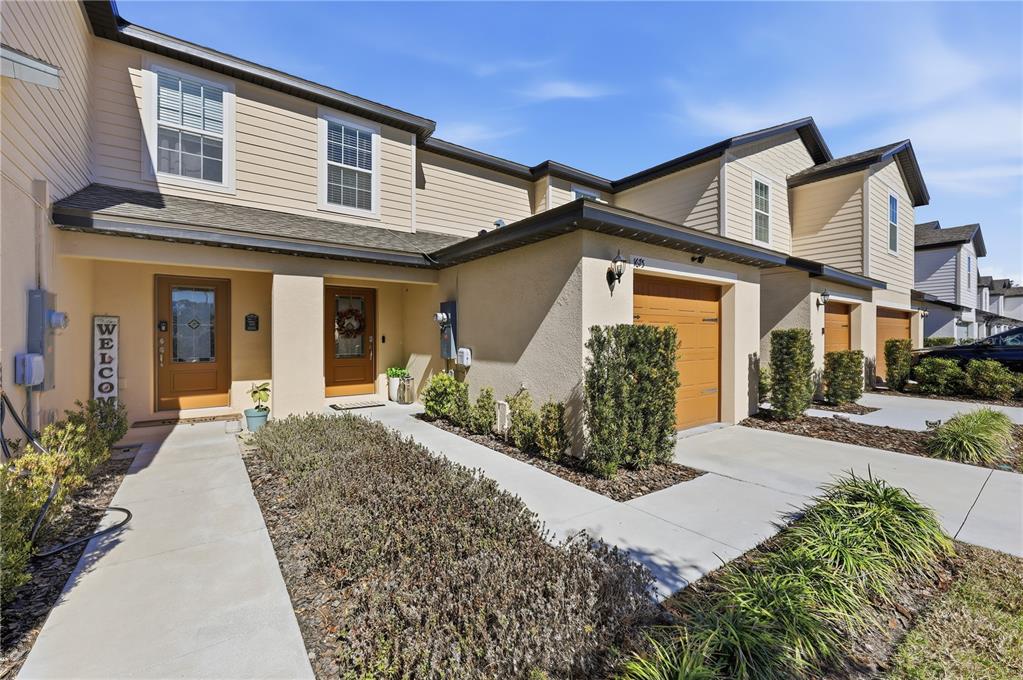 A row of two-story townhomes features beige siding, stucco facades, and attached single-car garages — 1675 WYNFORD CIRCLE, TAVARES, FL