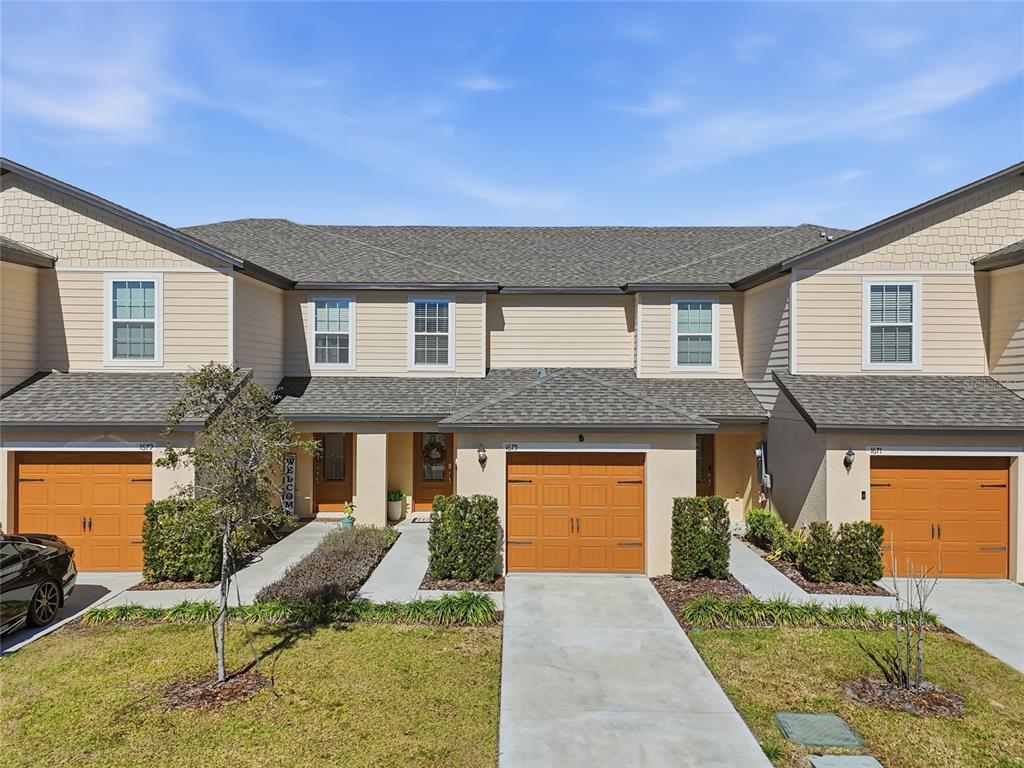 A row of three townhouses with beige siding, brown garage doors, and concrete driveways — 1675 WYNFORD CIRCLE, TAVARES, FL