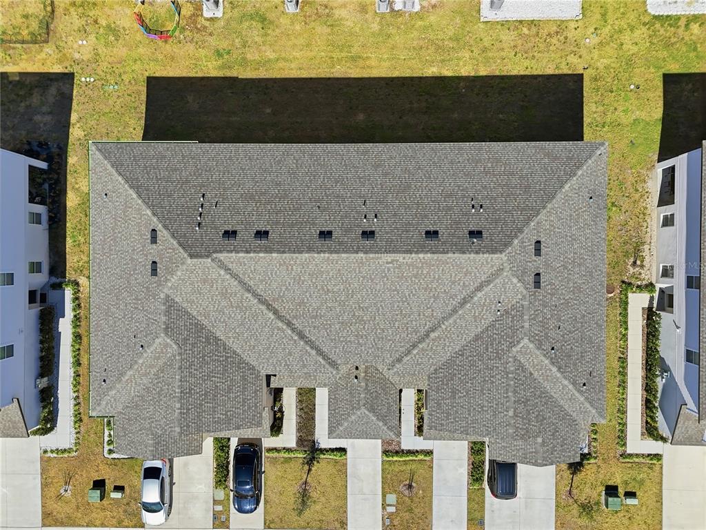 An aerial view shows the shingled roof of a multi-unit residential building with parked cars — 1675 WYNFORD CIRCLE, TAVARES, FL