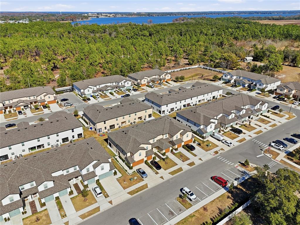 An aerial view shows a residential neighborhood of townhomes with parking spaces and surrounding woods — 1675 WYNFORD CIRCLE, TAVARES, FL