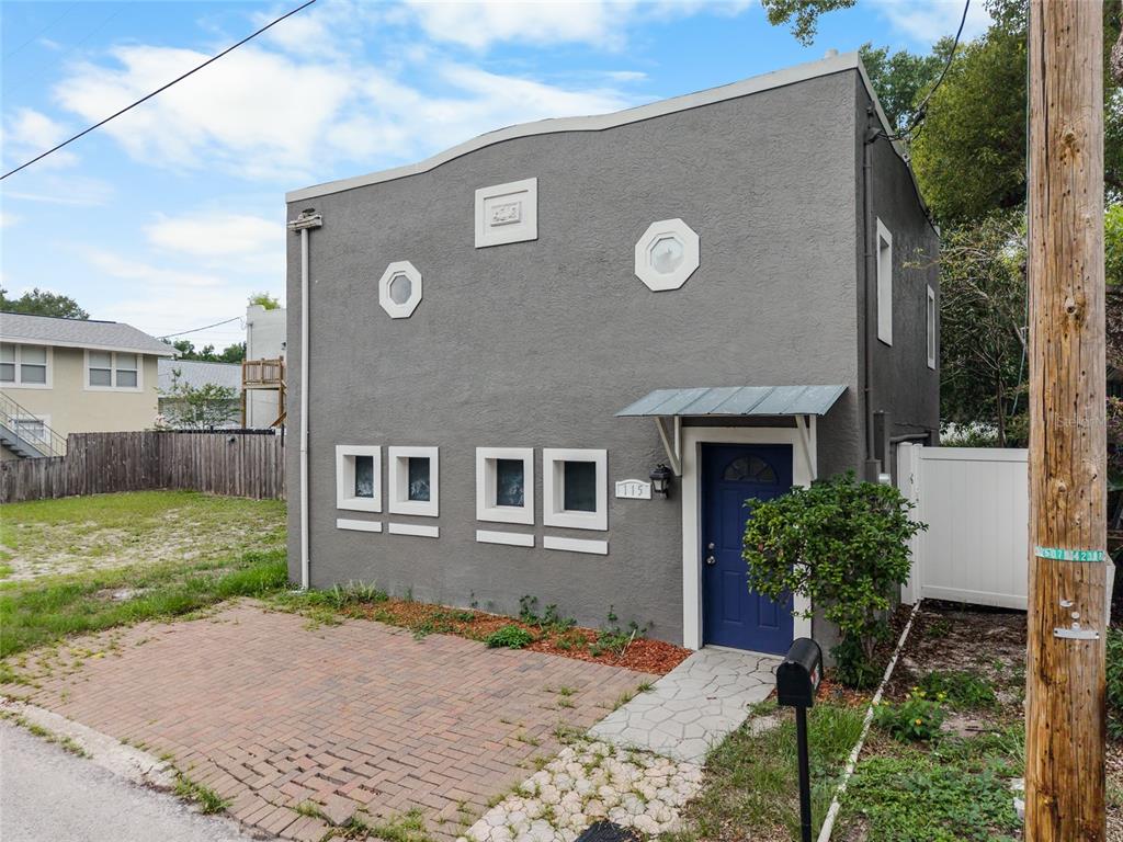 A two-story gray stucco building features a blue front door and a brick driveway — 115 W ALLISON COURT, TAMPA, FL