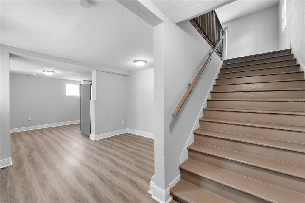 A staircase with brown wooden steps leads upward next to a room with light flooring — 115 W ALLISON COURT, TAMPA, FL