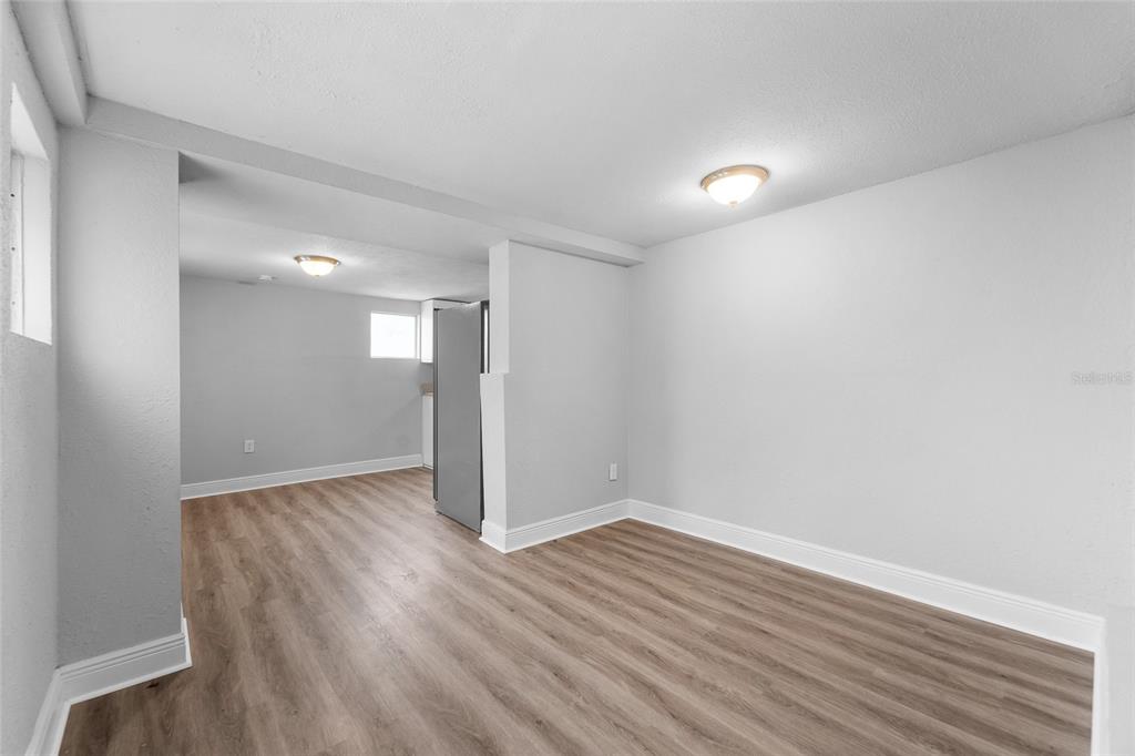 An interior view shows a room with light gray walls, wood-look flooring, and a refrigerator — 115 W ALLISON COURT, TAMPA, FL