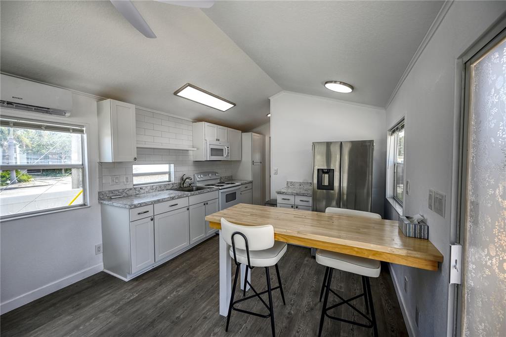 A kitchen features white cabinetry, a butcher block island, stainless steel appliances, and wood-look flooring — 6720 PARK BOULEVARD N UNIT 1, PINELLAS PARK, FL