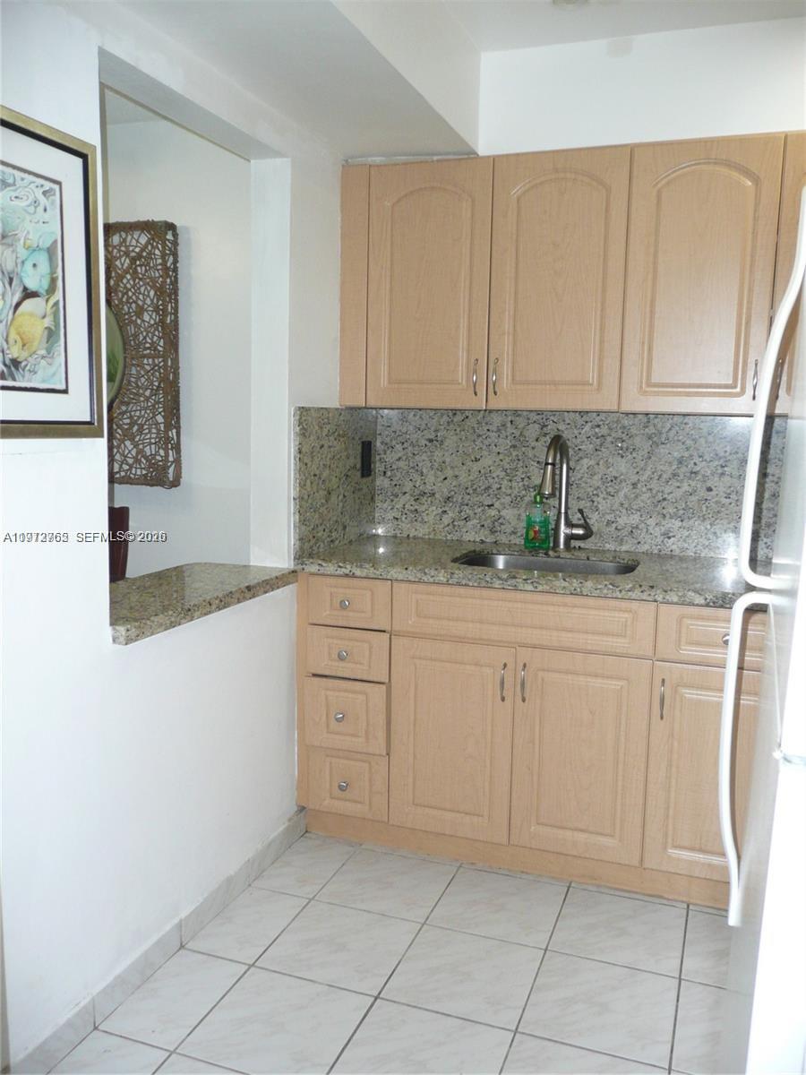 A small kitchen features light wood cabinets, granite countertops, and a stainless steel sink — SUNNY ISLES BEACH, FL