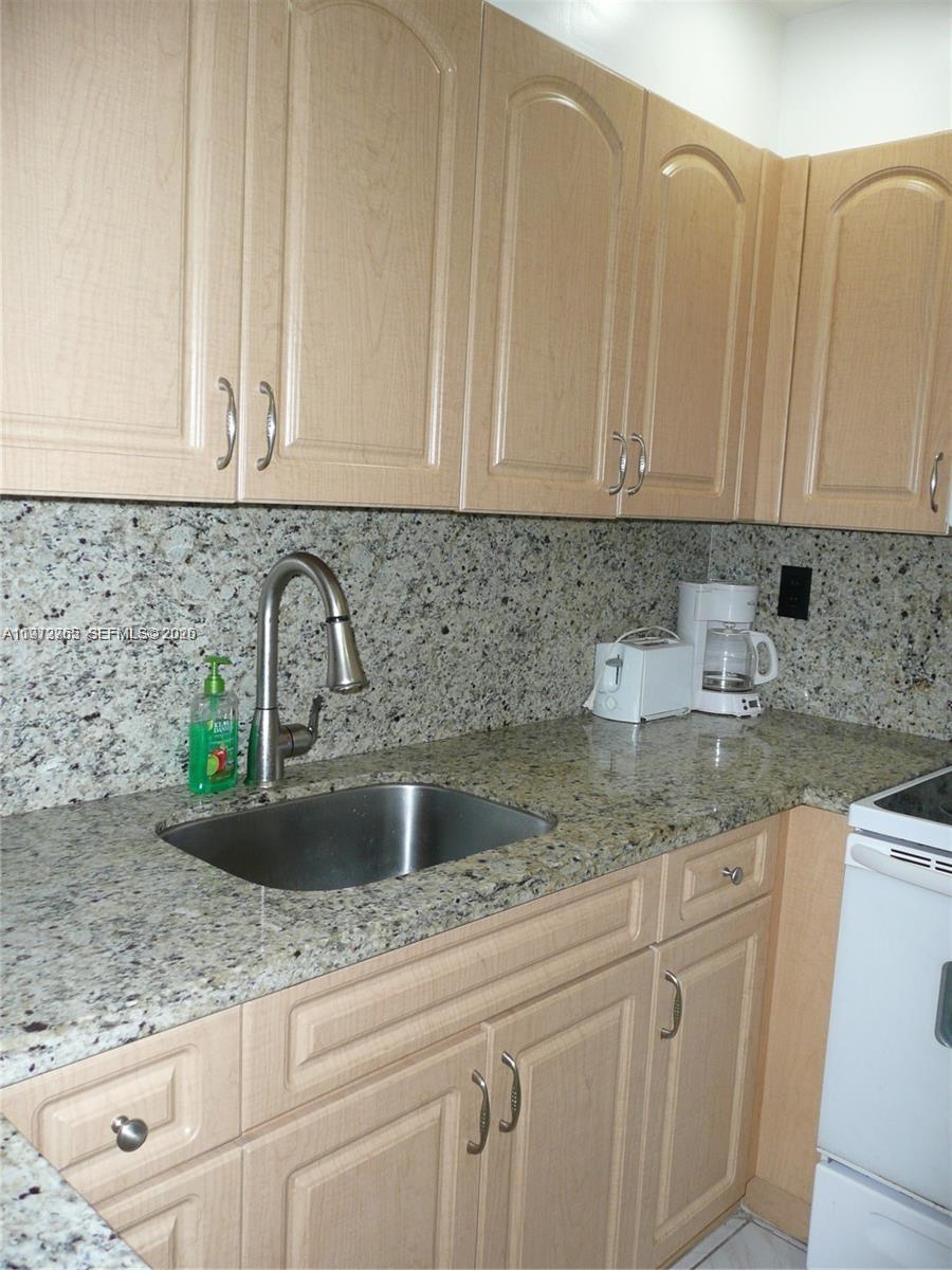 A kitchen features light wood cabinets, granite countertops, and a stainless steel sink — SUNNY ISLES BEACH, FL