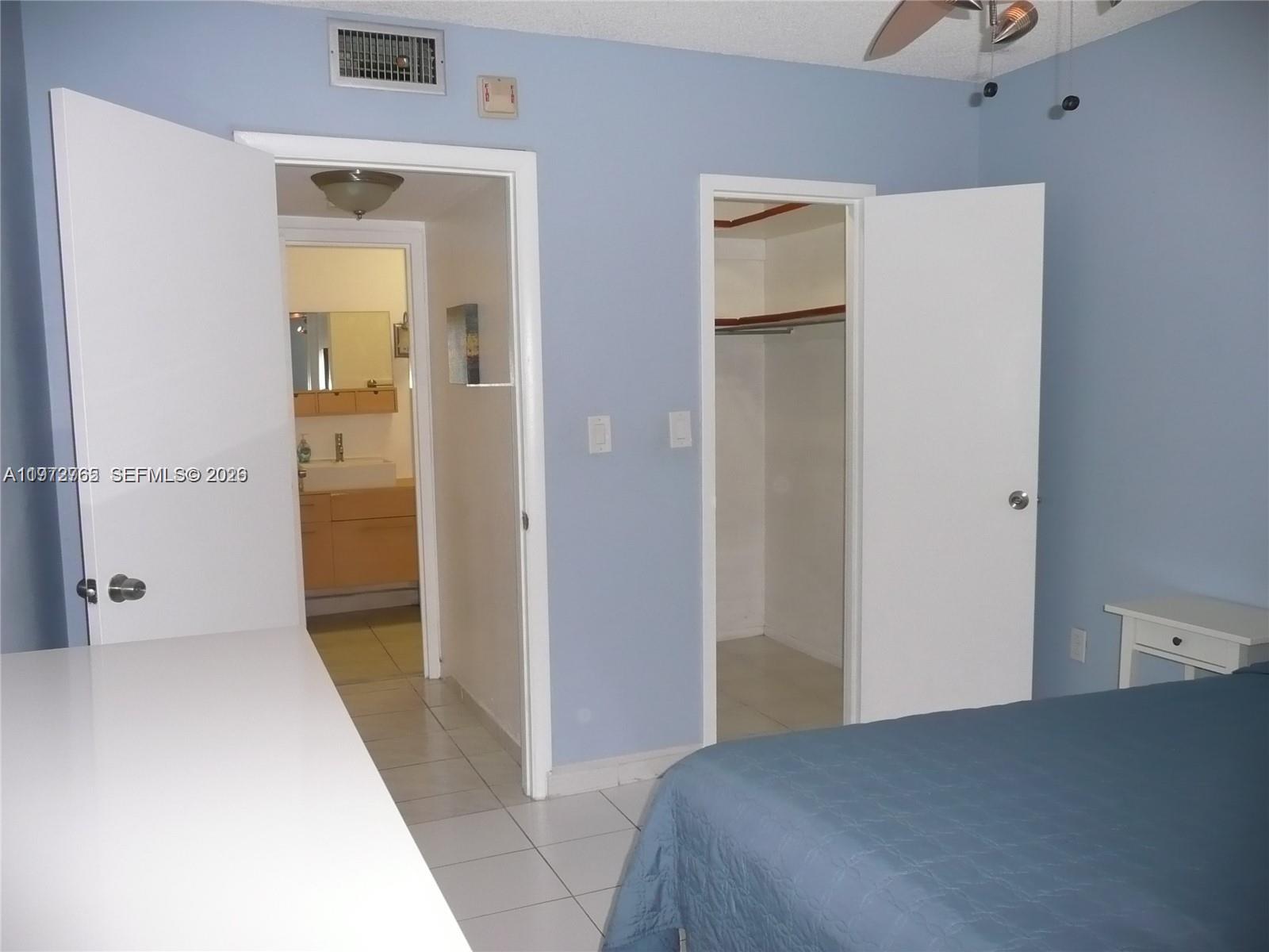 A bedroom features light blue walls, a white door to a bathroom, and a closet — SUNNY ISLES BEACH, FL