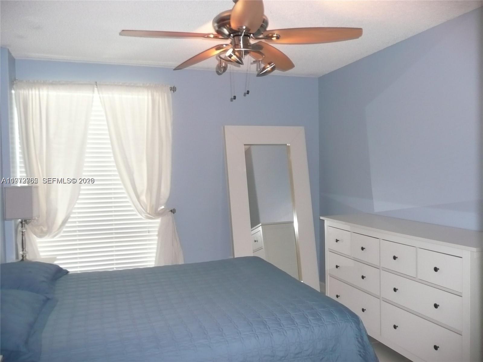 A bedroom features blue walls, a white dresser, a floor mirror, and a ceiling fan — SUNNY ISLES BEACH, FL