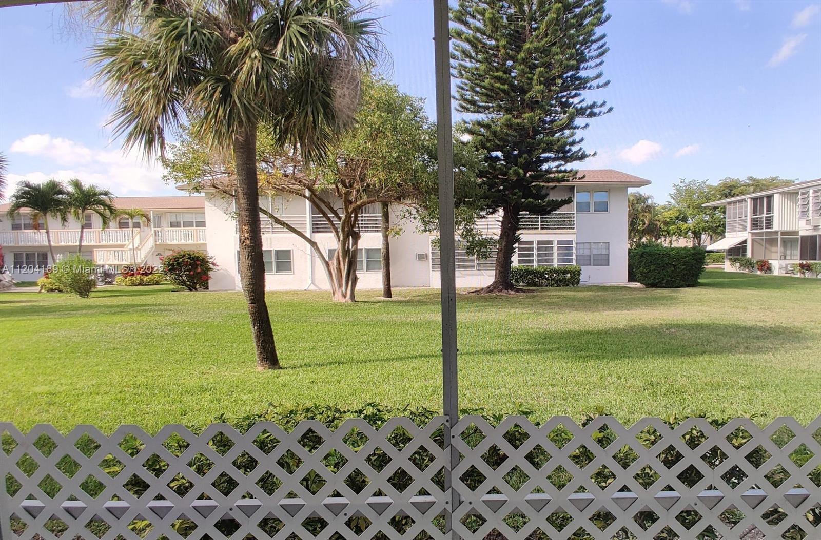 A view of a grassy courtyard with palm trees and apartment buildings from a screened-in porch — 155 Easthampton G # 155, West Palm Beach FL 33417, WEST PALM BEACH, FL