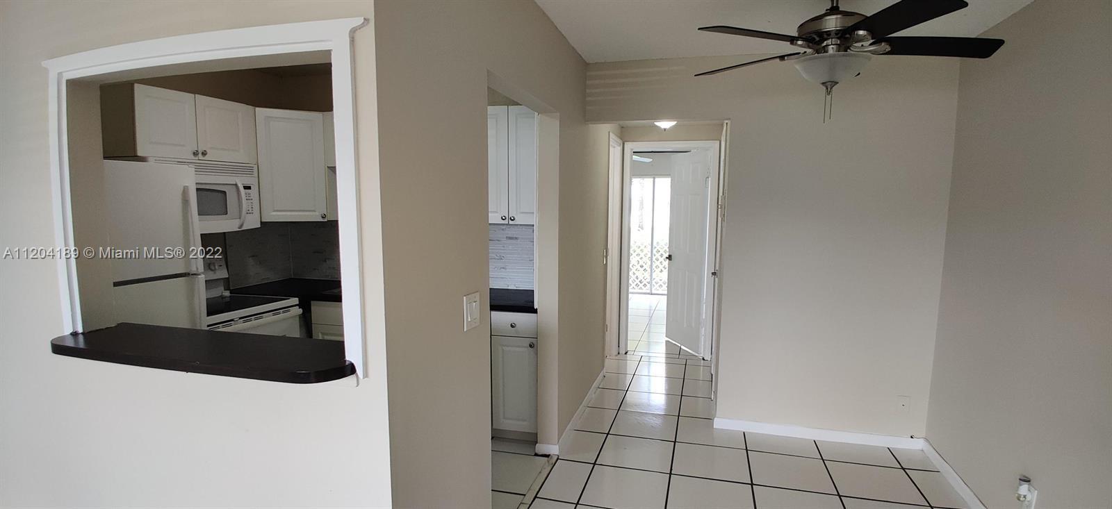 A kitchen with white cabinets and a pass-through window opens into a tiled dining area — 155 Easthampton G # 155, West Palm Beach FL 33417, WEST PALM BEACH, FL