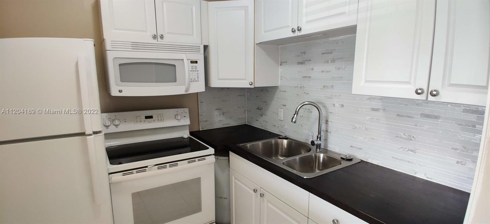 A kitchen features white cabinets, a white stove, a microwave, and a dark countertop — 155 Easthampton G # 155, West Palm Beach FL 33417, WEST PALM BEACH, FL