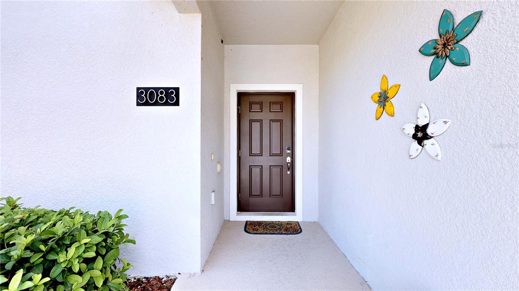 A brown front door with a house number sign and decorative wall flowers — 3083 TOM SAWYER DRIVE, KISSIMMEE, FL
