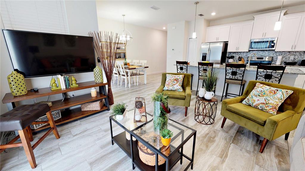 An open-concept living room and kitchen feature tile flooring, olive green armchairs, and white cabinetry — 3083 TOM SAWYER DRIVE, KISSIMMEE, FL