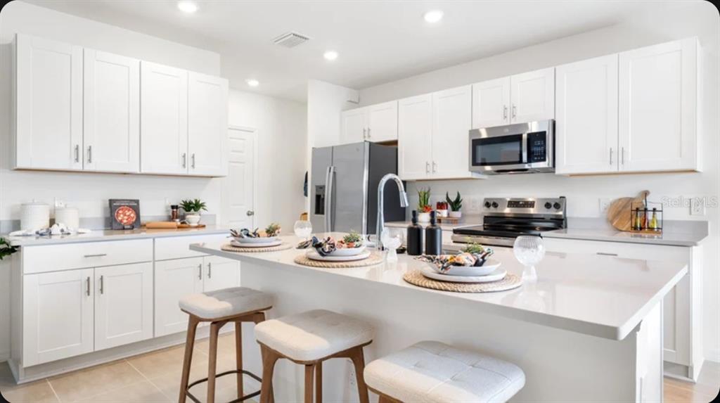 A bright kitchen features white cabinetry, stainless steel appliances, and a large central island — 13966 BLUSTERY COURT, HUDSON, FL