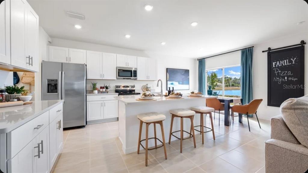 A modern kitchen features white cabinetry, stainless steel appliances, a center island, and dining area — 13966 BLUSTERY COURT, HUDSON, FL