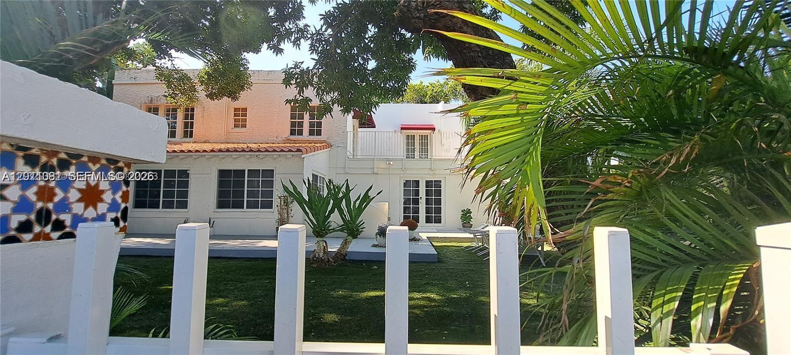 A white two-story house with a backyard, lawn, and palm trees viewed through a fence — 846 Michigan Ave # 101, Miami Beach FL 33139, MIAMI BEACH, FL