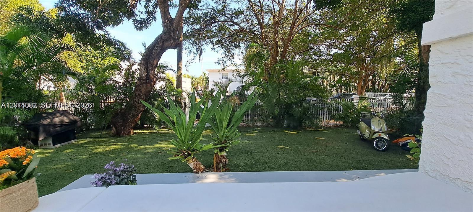 A view of a grassy backyard with trees, a scooter, and a grill — 846 Michigan Ave # 101, Miami Beach FL 33139, MIAMI BEACH, FL