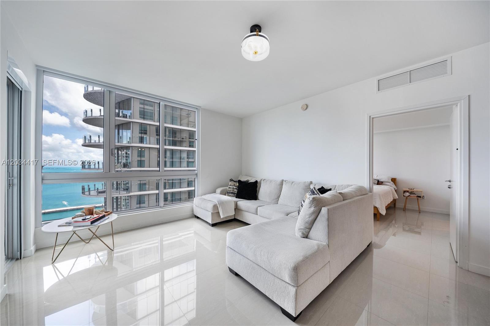A living room with a sectional sofa, white tile floors, and floor-to-ceiling windows overlooking water — 300 S Biscayne Blvd # 3406, Miami FL 33131, MIAMI, FL