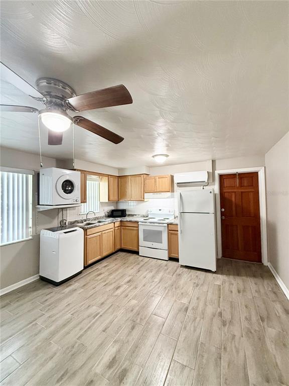 A kitchen features wood cabinets, white appliances, a stacked washer-dryer unit, and light wood-look flooring — 38839 3RD AVENUE, ZEPHYRHILLS, FL