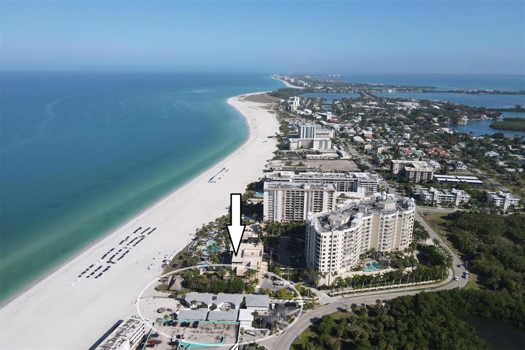 An aerial view shows a beachfront resort complex with a white arrow pointing toward buildings — 1336 BENJAMIN FRANKLIN DRIVE UNIT F2, SARASOTA, FL