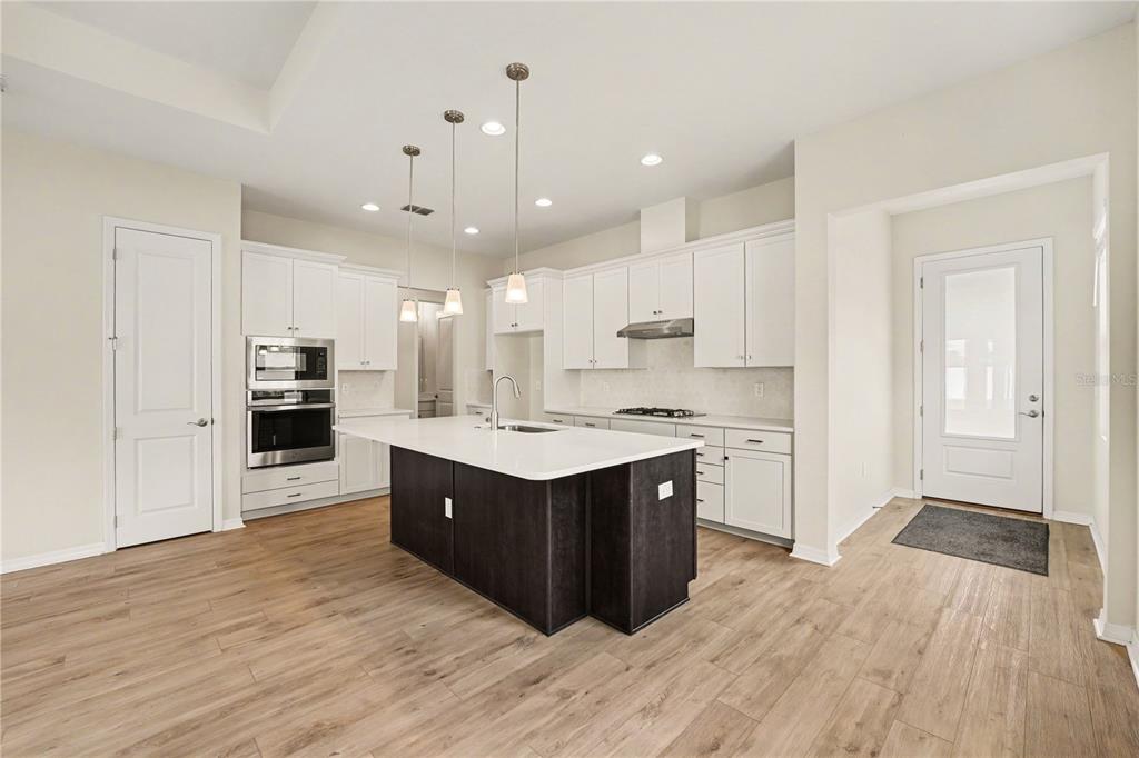 A modern kitchen features white cabinetry, a dark island, stainless appliances, and light wood flooring — 1991 KEY BAY TRAIL, KISSIMMEE, FL