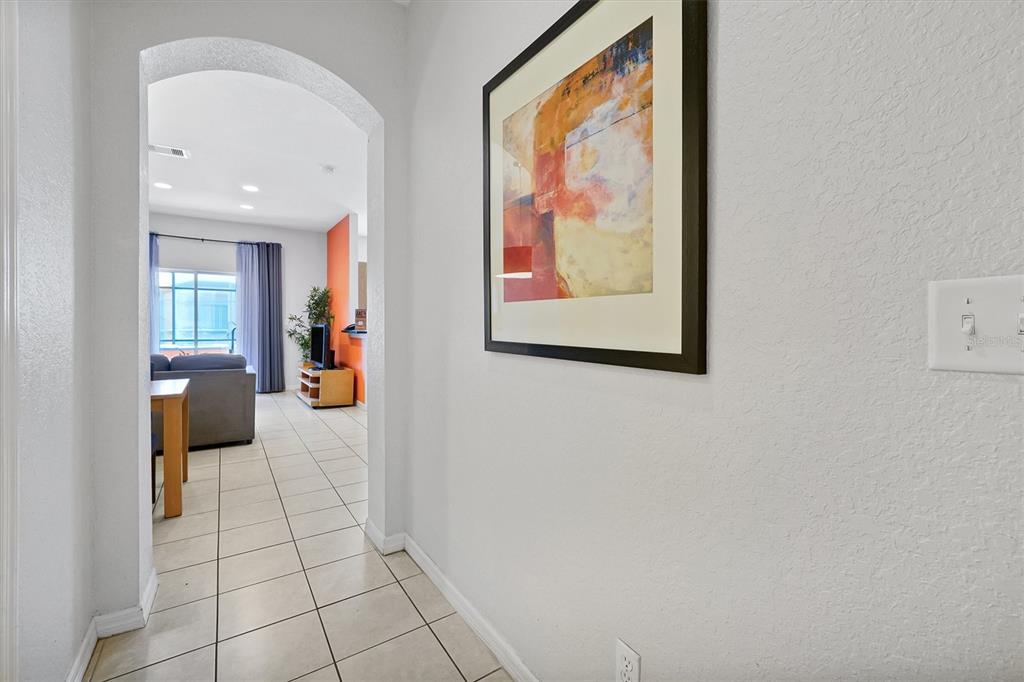 A tiled hallway leads through an arched doorway into a living room with orange walls — 2724 COUPE STREET, KISSIMMEE, FL