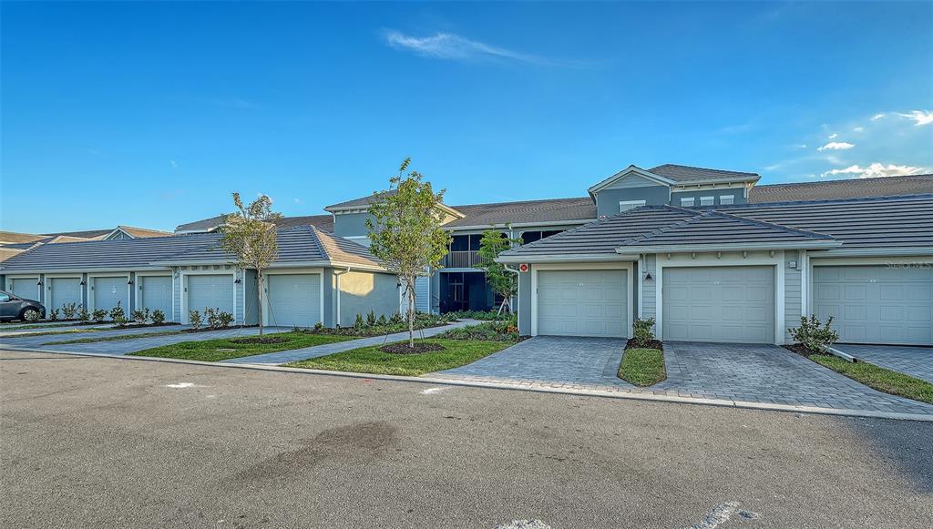 A row of attached residential garages with gray doors and paved driveways under a blue sky — 17500 OPAL SAND DRIVE UNIT 205, VENICE, FL