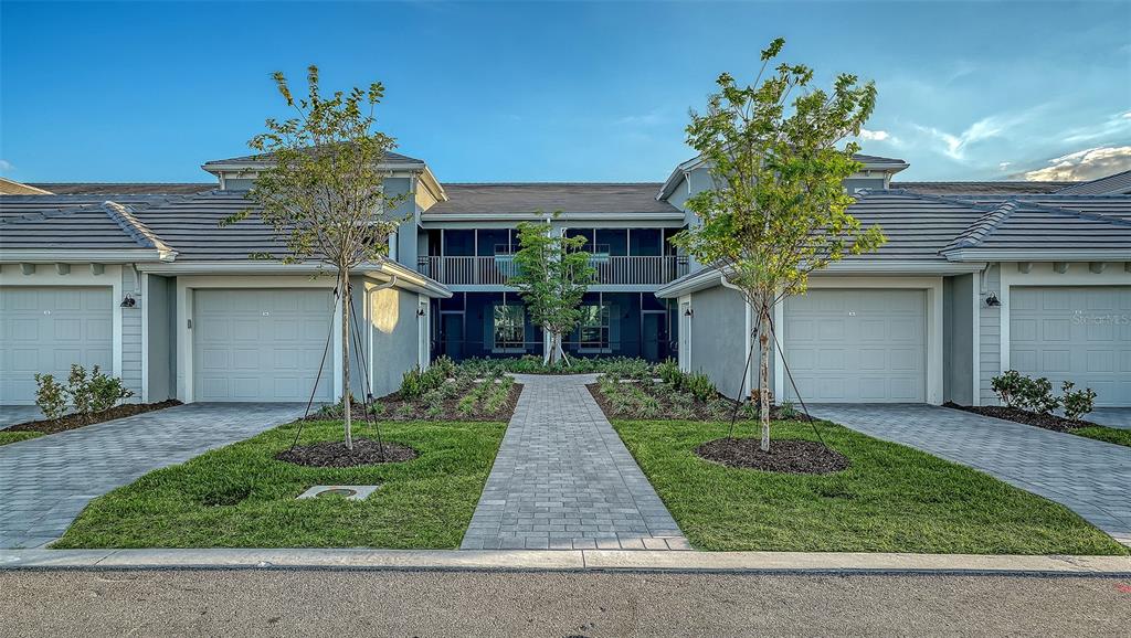 A two-story residential building features two garages, a central walkway, and a screened upper balcony — 17500 OPAL SAND DRIVE UNIT 205, VENICE, FL