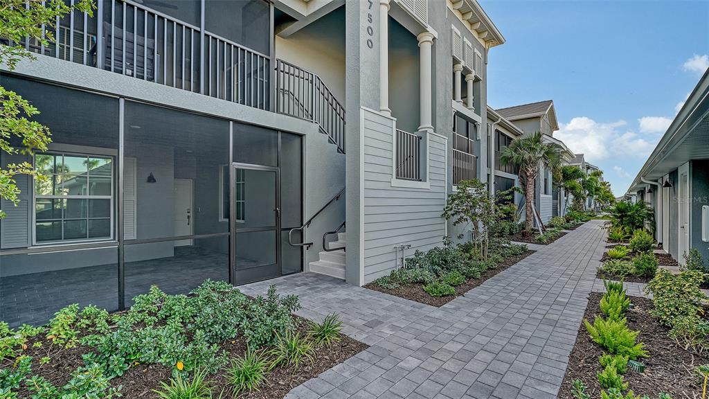 A multi-story apartment building exterior features a screened-in patio, stairs, and a paved walkway — 17500 OPAL SAND DRIVE UNIT 205, VENICE, FL