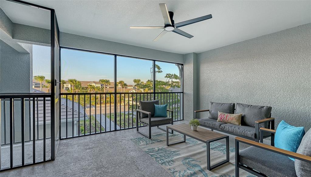 A screened-in balcony features gray patio furniture, a patterned rug, and a ceiling fan — 17500 OPAL SAND DRIVE UNIT 205, VENICE, FL