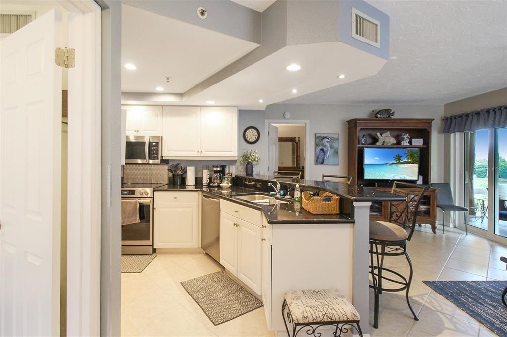 A kitchen with white cabinets and black countertops opens into a living area with tile — 1364 SIESTA BAYSIDE DRIVE UNIT 1364-C, SARASOTA, FL