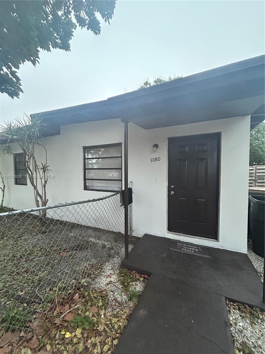 A white exterior wall features a dark brown front door and a small window — 1080 NW 121st St, North Miami FL 33168, NORTH MIAMI, FL