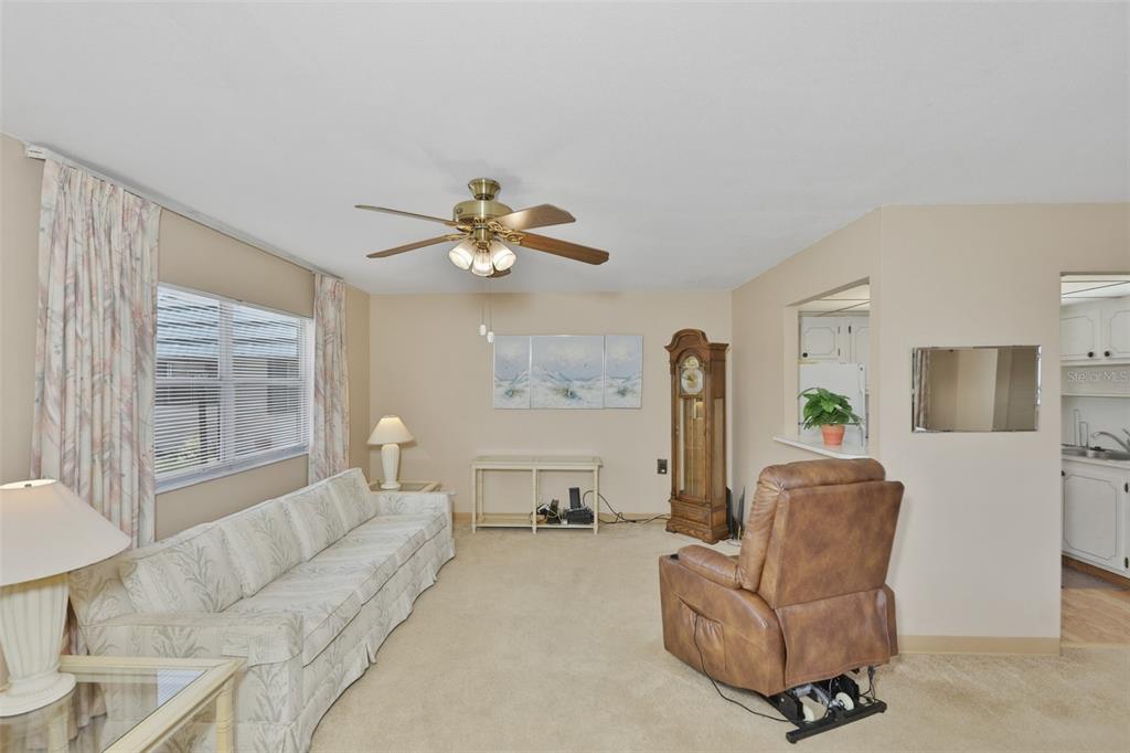 A living room features beige carpeting, a sofa, a recliner, and a grandfather clock — 1811 BEDFORD LANE UNIT 163, SUN CITY CENTER, FL