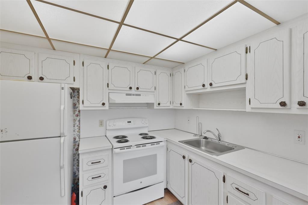 A kitchen features white cabinets, a white stove, a refrigerator, and a drop ceiling — 1811 BEDFORD LANE UNIT 163, SUN CITY CENTER, FL