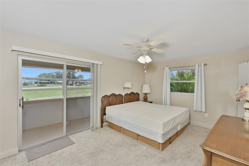 A bedroom features a bed, a ceiling fan, a sliding glass door, and carpeted flooring — 1811 BEDFORD LANE UNIT 163, SUN CITY CENTER, FL