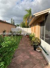 A paved walkway leads alongside a house toward a white fence in a backyard — 11882 SW 209th Ter, Miami FL 33177, MIAMI, FL