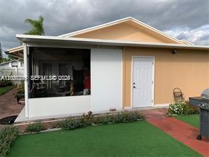 A tan house features a screened-in patio, a white door, and a green lawn — 11882 SW 209th Ter, Miami FL 33177, MIAMI, FL