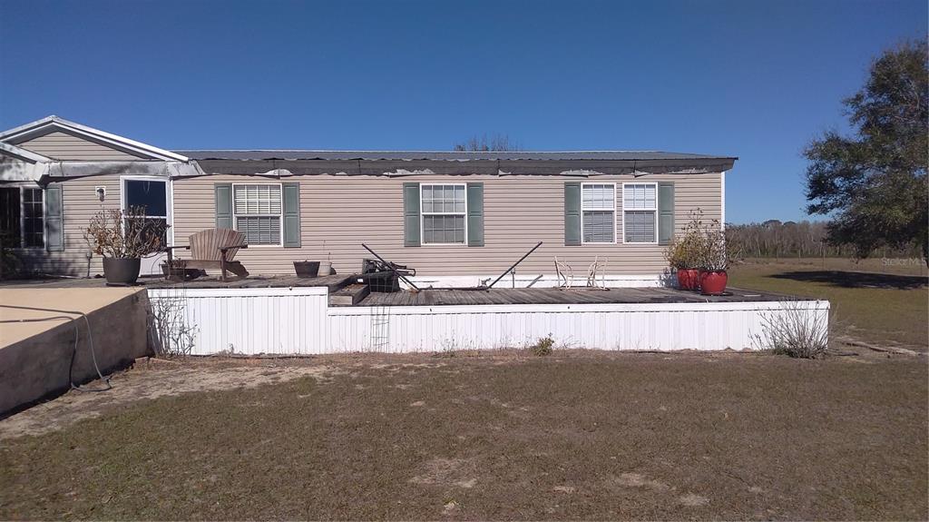A single-story manufactured home features light-colored siding, a large wooden deck, and white skirting — 12051 AVON PARK CUT OFF ROAD, FORT MEADE, FL